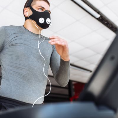 beautiful pumped up young man, engaged in sports, in training mask for breathing on the treadmill, morning training