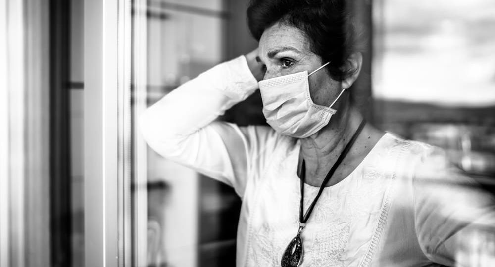 Senior elderly sad woman at home looking through the window.Coro