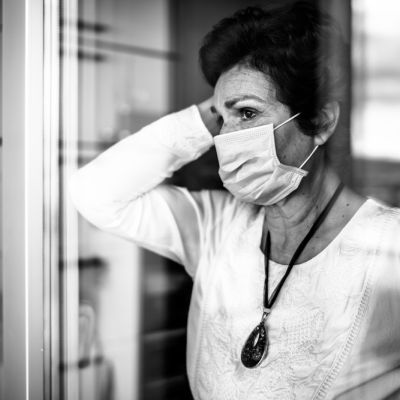 Senior elderly sad woman at home looking through the window.Coro