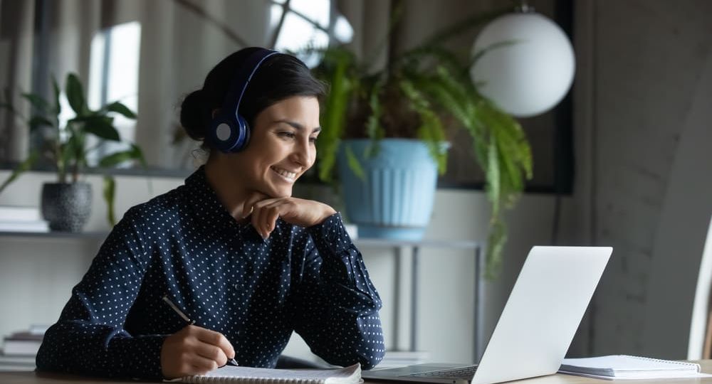 Happy young indian girl with headphones looking at laptop screen.