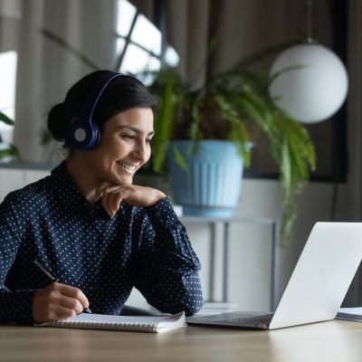 Happy young indian girl with headphones looking at laptop screen.